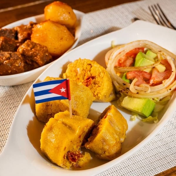 Cuban meal with meat and potatoes, plantain fritters, and a fresh salad with avocado and onions.