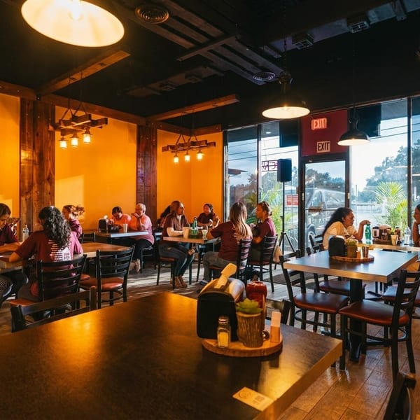 Diners seated at tables in a warmly lit restaurant with orange walls and wooden accents.