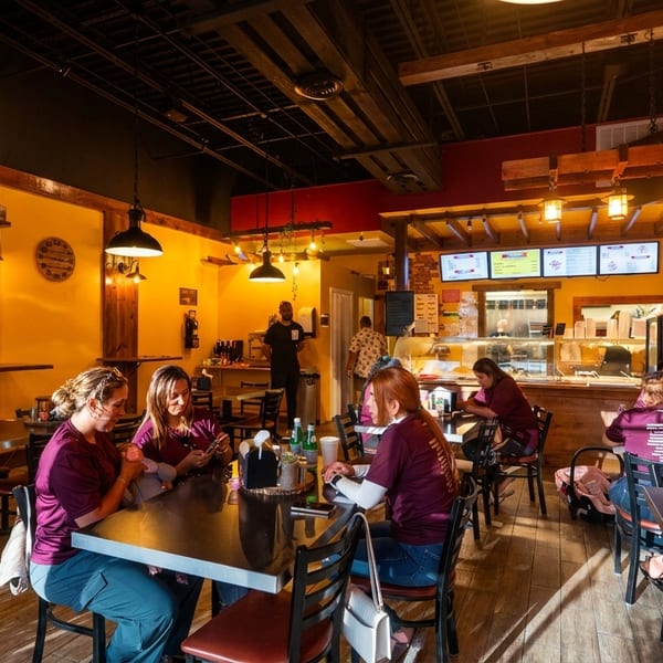 A vibrant restaurant interior with patrons dining at tables, a counter service area, and warm lighting.